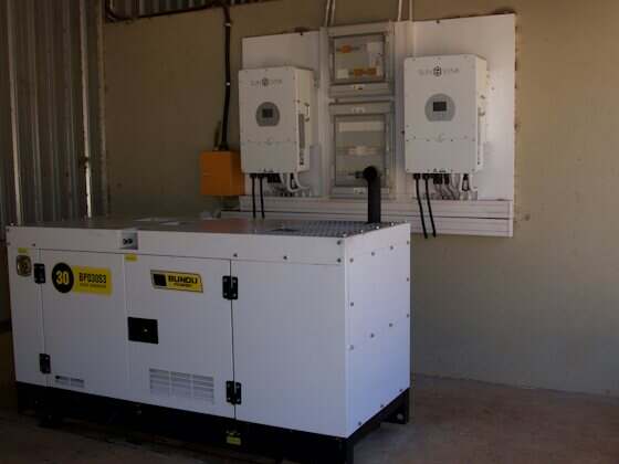 Gerador silenciado branco instalado ao lado de quadros elétricos
