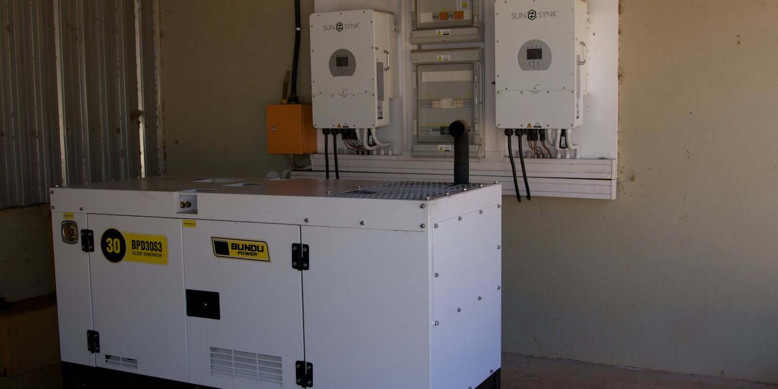 Gerador silenciado branco instalado ao lado de quadros elétricos