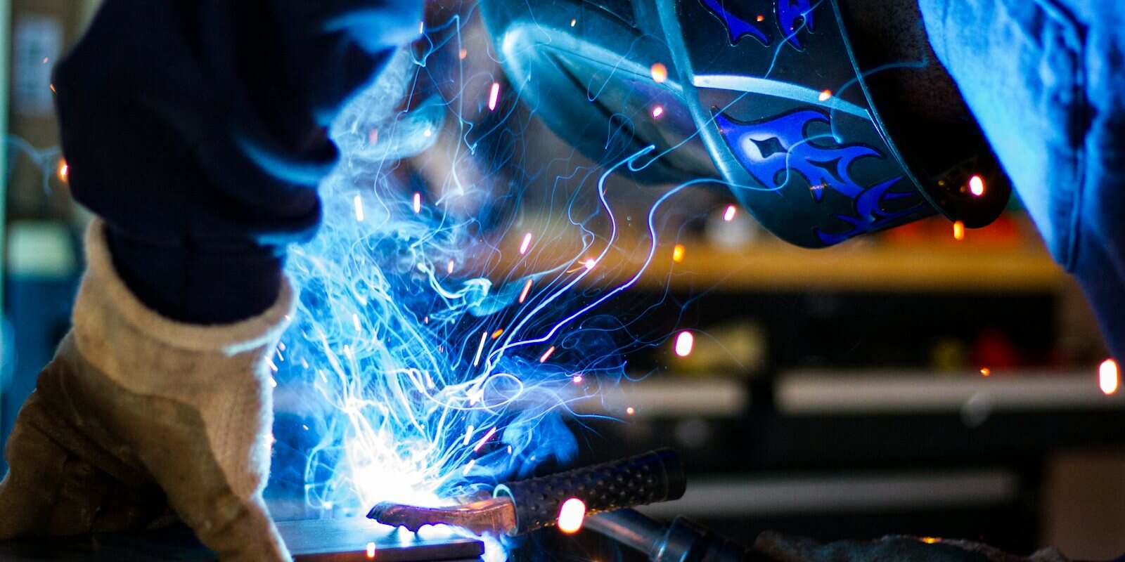 Soldador com máscara e luvas soldando metal, com faíscas