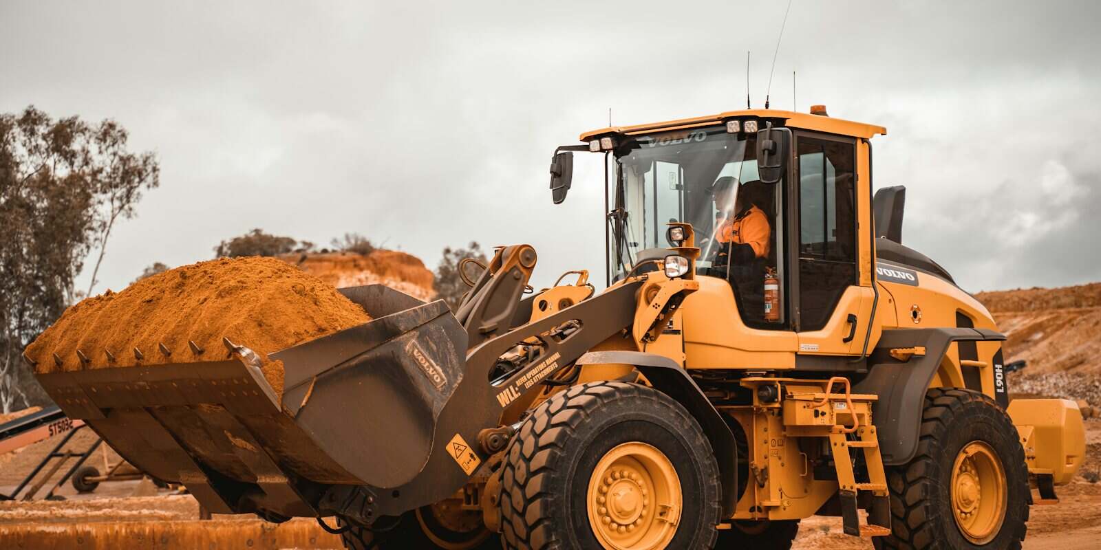 Pá carregadeira amarela erguendo a caçamba cheia de terra