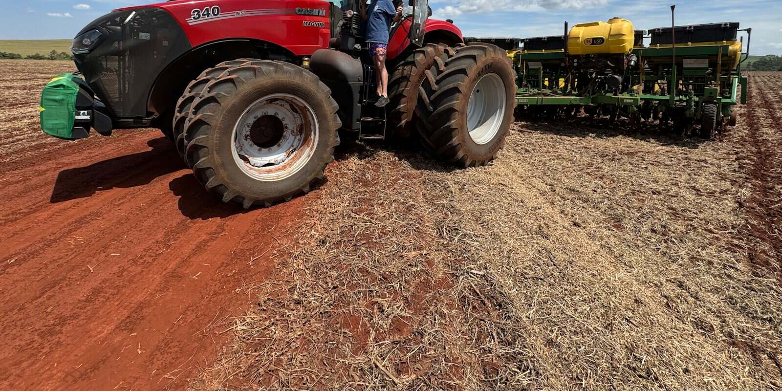 Trator vermelho com plantadeira acoplada em solo preparado