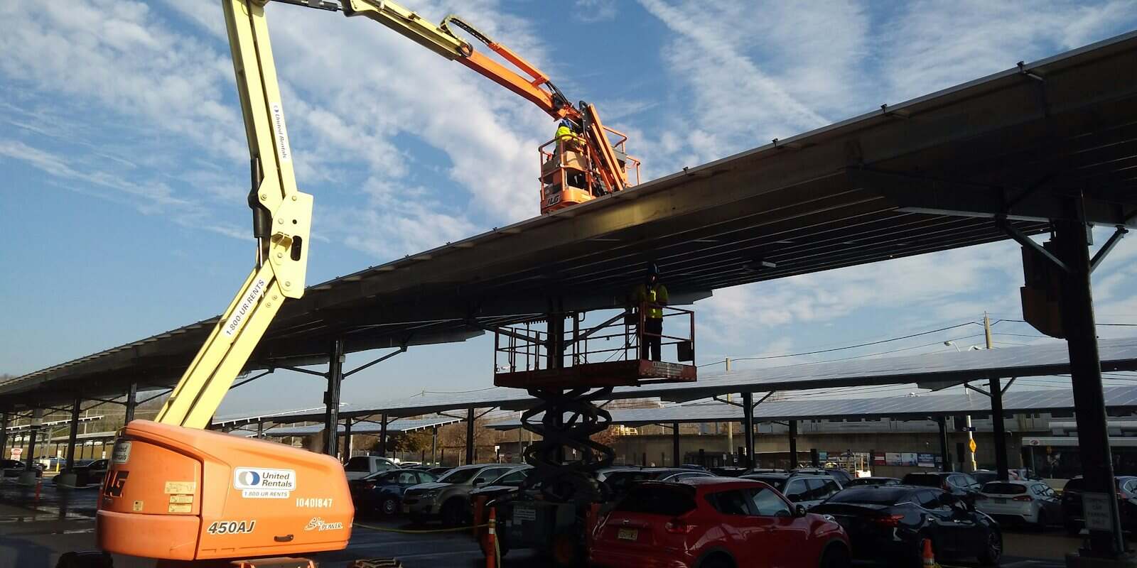 Plataforma elevatória articulada com a cesta erguida junto a uma cobertura metálica