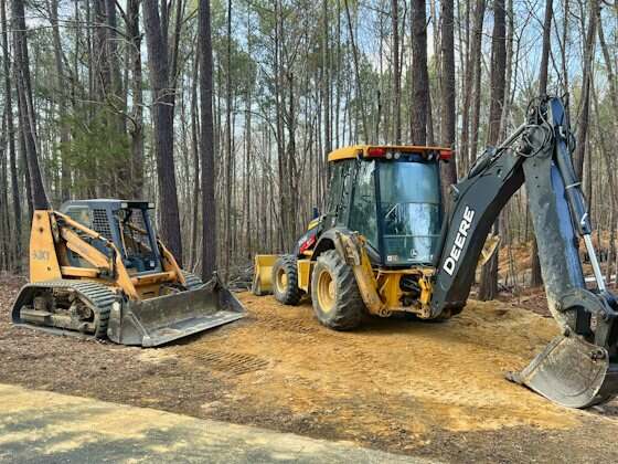 Retroescavadeira John Deere e uma minicarregadeira num terreno em obra