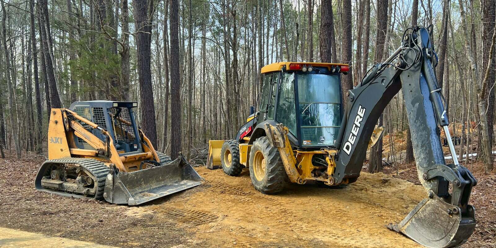 Retroescavadeira John Deere e uma minicarregadeira num terreno em obra