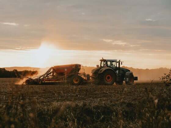 Trator agrícola puxando implemento ao entardecer