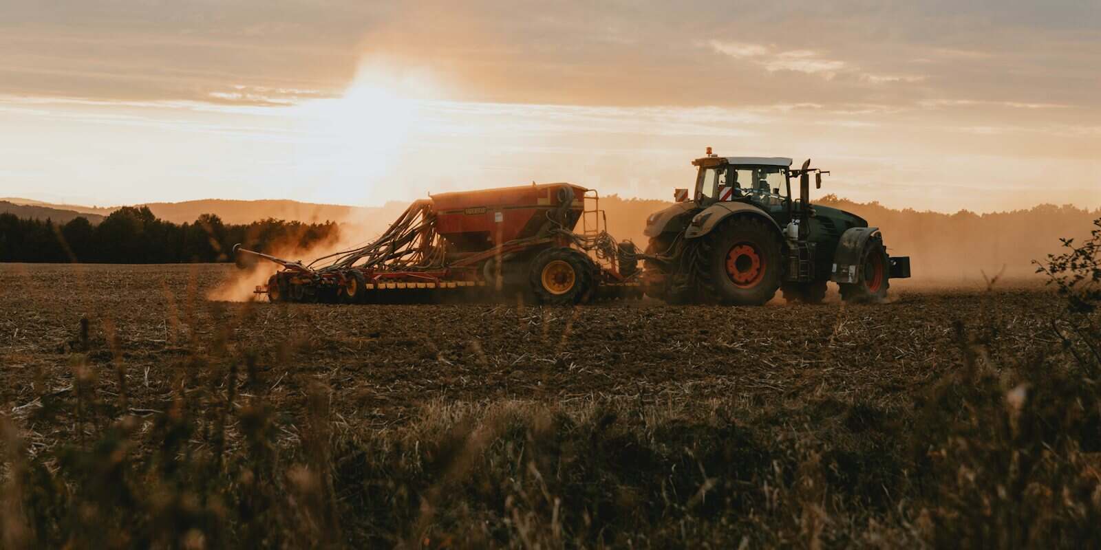 Trator agrícola puxando implemento ao entardecer